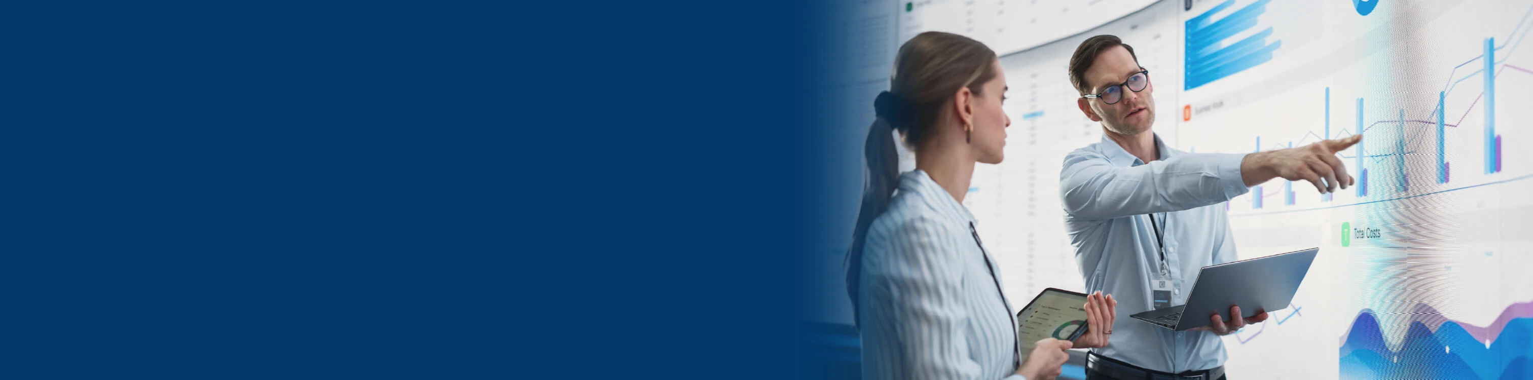 Image of two professionals analysing data and pointing at a large screen