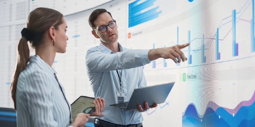 Image of two professionals analysing data and pointing at a large screen