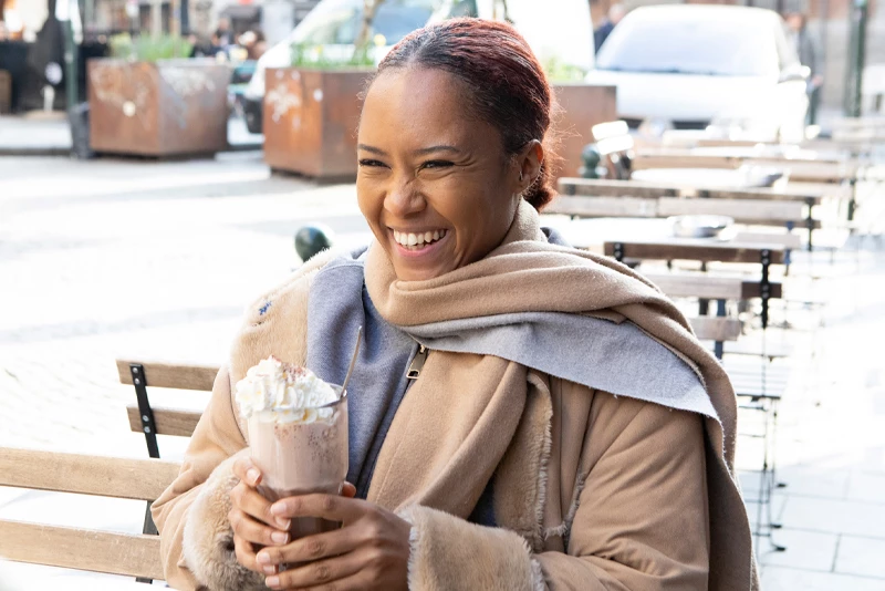 Image of a woman similing while walking down the street holding a coffee