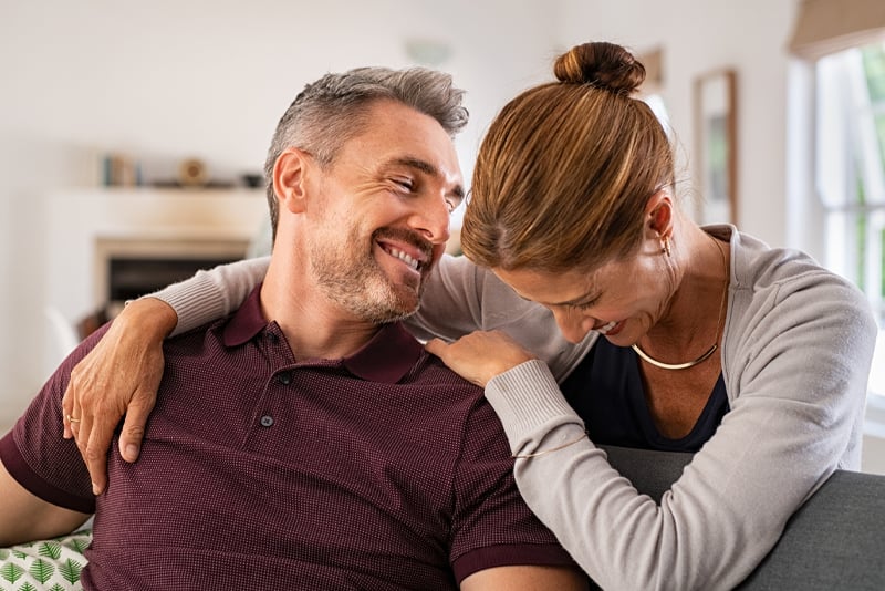 A husband and wife hugging together on a couch