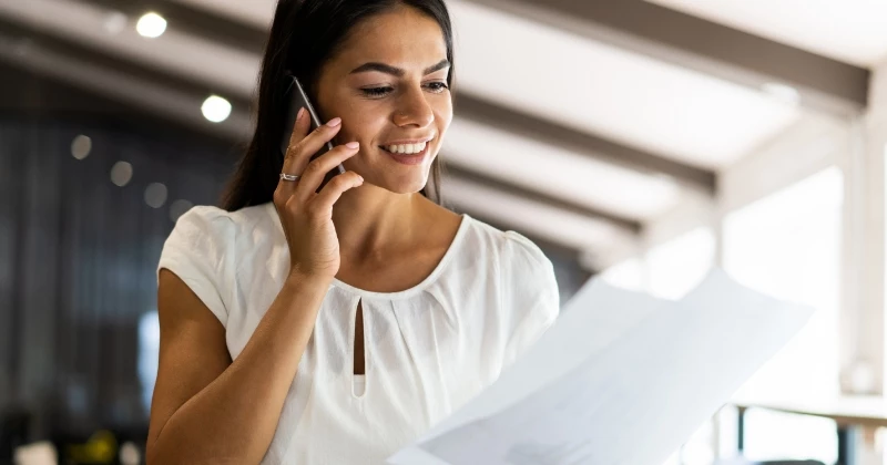 Image of a woman smiling on the phone while looking at a bill in her hand