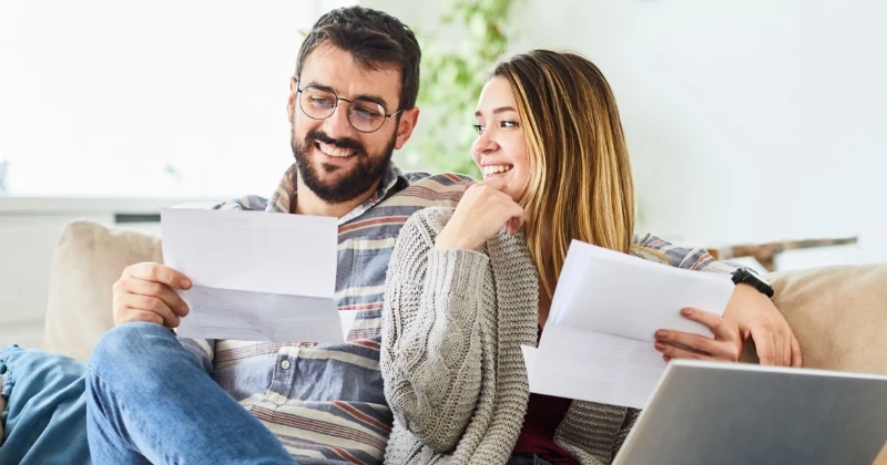 Image of a couple sitting on the couch smiling and looking at bills