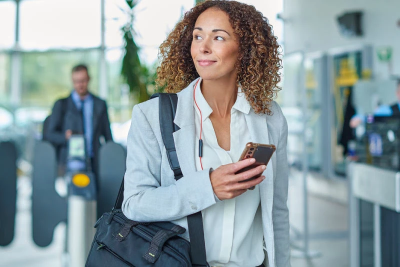 A young woman looks over her right shoulder while walking with her phone in her hand
