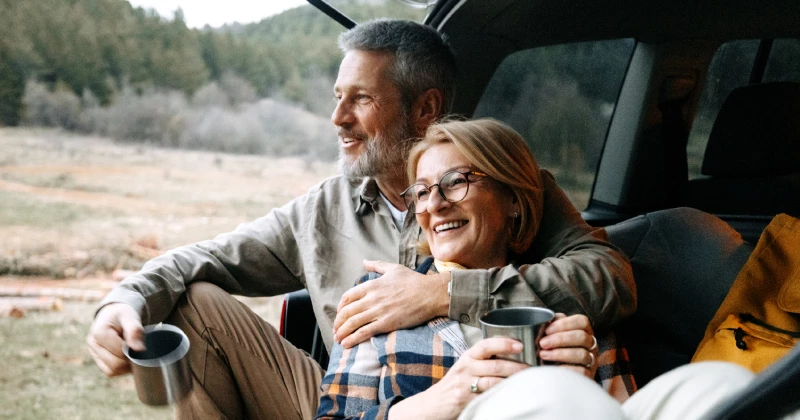 Image of a couple camping and sitting in the trunk of their car