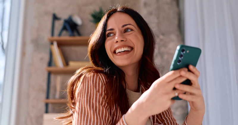 Image of a woman smiling while holding her mobile phone