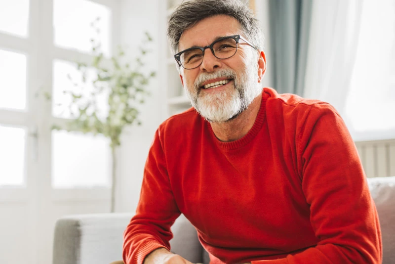 Image of an older man smiling while sitting inside on a chair