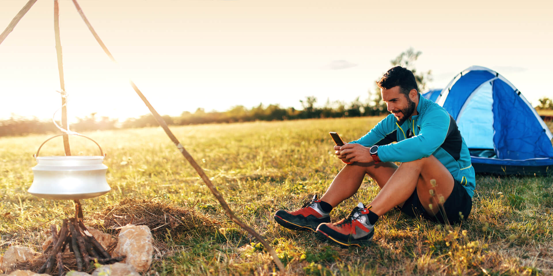 A relaxed man who is sitting outside a tent at a campsite checks his online bank accounts from his phone