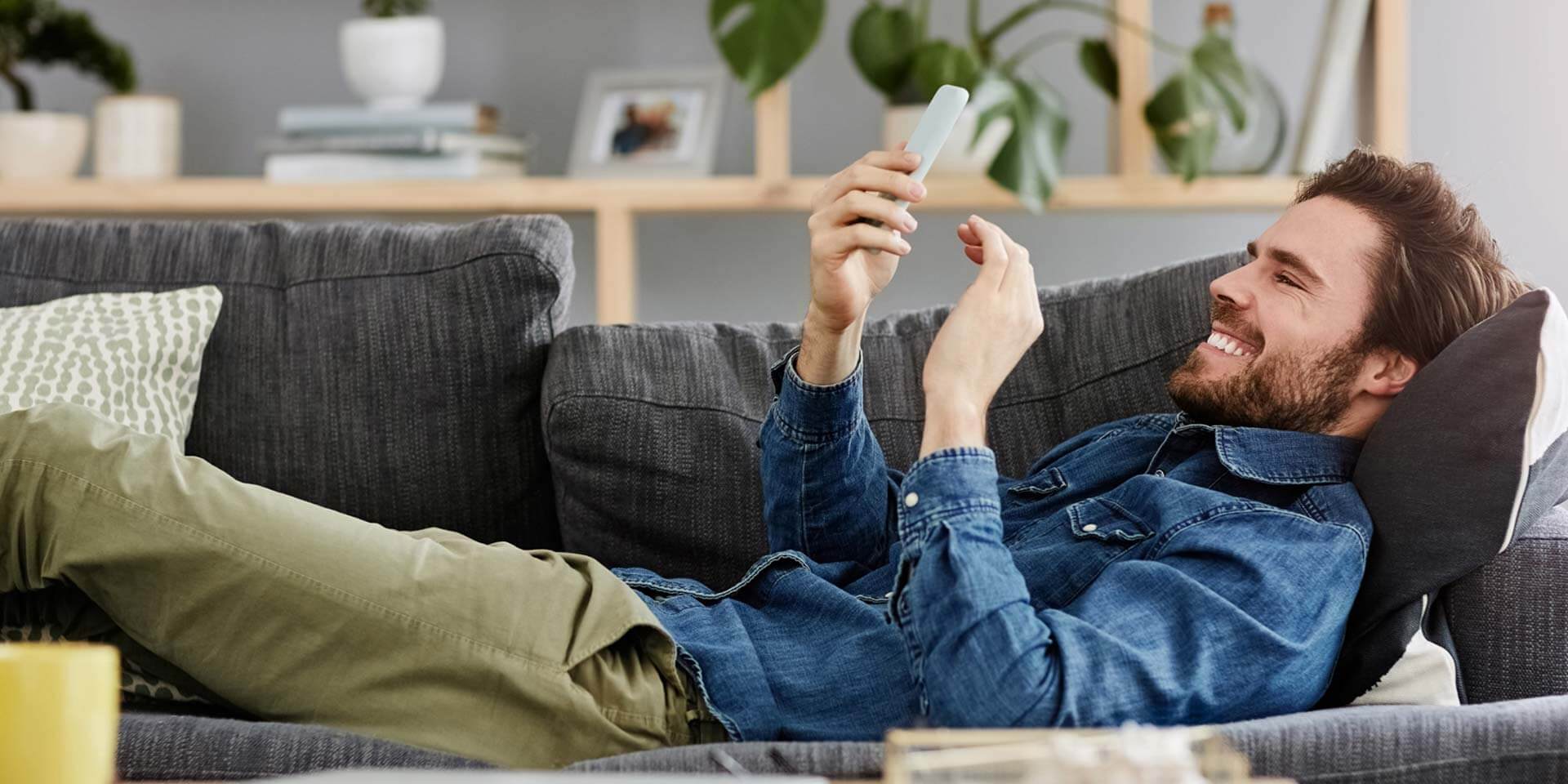 A man lays back on his sofa and uses Zelle to send money to a friend