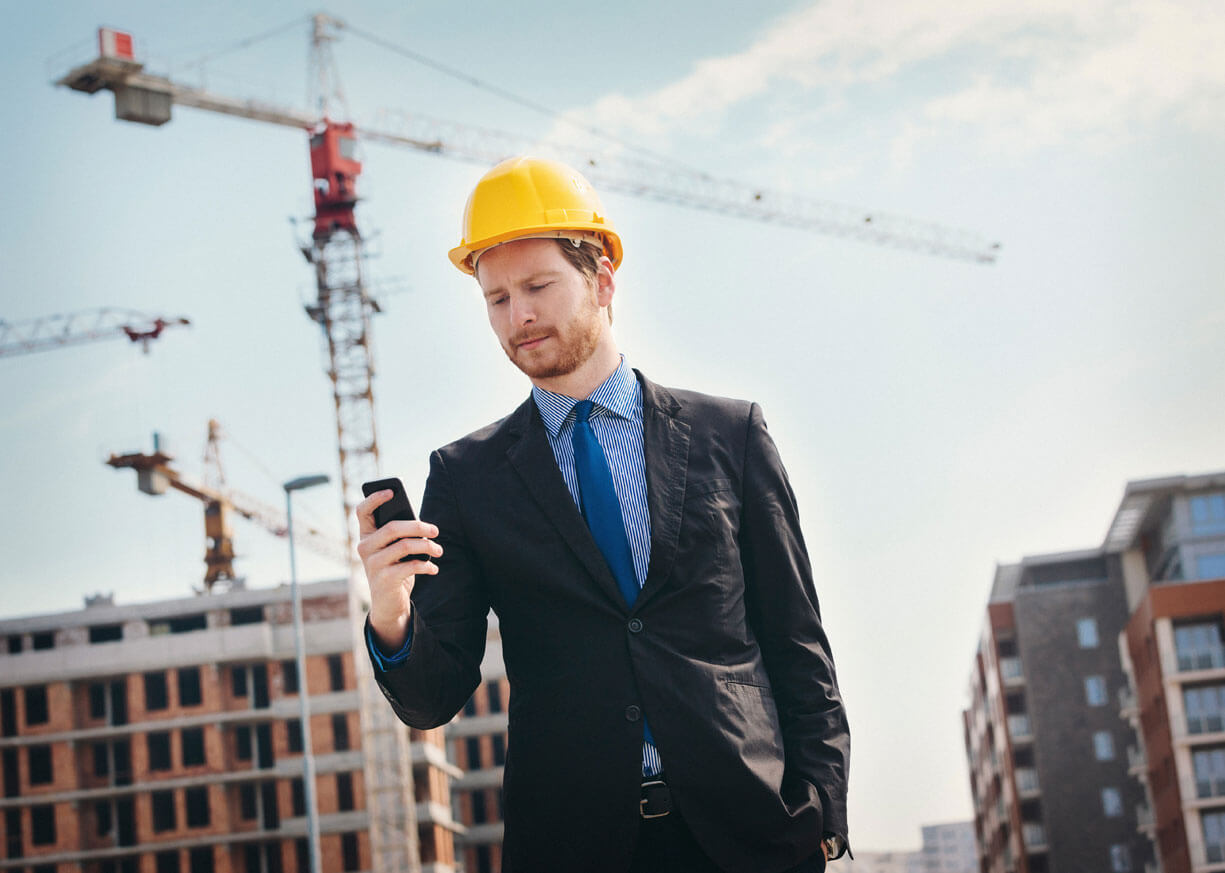 A businessman at a busy construction site looks at his phone and considers his commercial banking and loan options