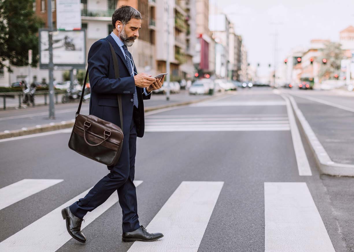 A businessman crosses the street with a briefcase and tablet while considering his Commercial Banking options