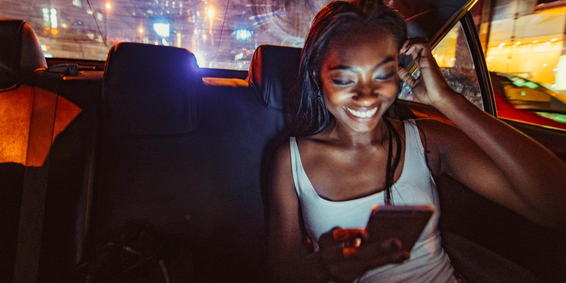 A young woman in the back seat of a car smiles while making digital payments from her phone