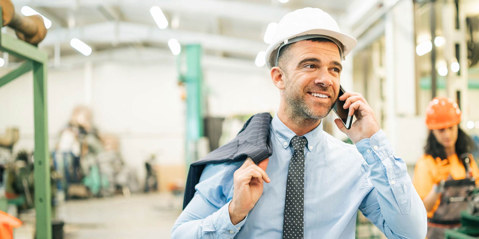 A business manager who received a Term Loan for his business talks on a cell phone while wearing a hard hat in a warehouse