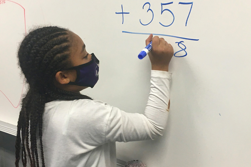 A girl solving a math equation on a white board